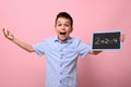 An adorable boy, an elementary school student, holds a chalk and a chalkboard and happily solves math problems. Pink background