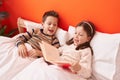 Adorable boy and girl reading book sitting on bed at bedroom Royalty Free Stock Photo