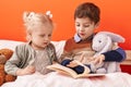 Adorable boy and girl reading book sitting on bed at bedroom Royalty Free Stock Photo