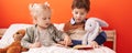 Adorable boy and girl reading book sitting on bed at bedroom Royalty Free Stock Photo