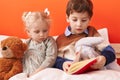 Adorable boy and girl reading book sitting on bed at bedroom Royalty Free Stock Photo