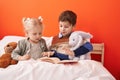 Adorable boy and girl reading book sitting on bed at bedroom Royalty Free Stock Photo