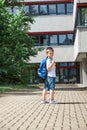 Adorable boy goes to school after vacation. A schoolboy with a backpack is standing and waving to his parents. Back to school,