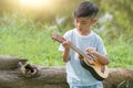 Adorable boy with guitar sitting on the grass on sunset, Musical concept with little boy playing ukulele at sunny park