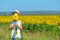 Adorable boy in hat hiding behind sunflower on yellow field outdoors