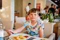 Adorable boy having breakfast at resort restaurant. Happy school kid child eating healthy food, vegetables and eggs in Royalty Free Stock Photo