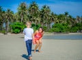 Adorable boy having fun with his mom on the tropical beach. White t-shirt, dark trousers and sunglasses. Barefoot on white sand. Royalty Free Stock Photo