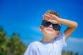 Adorable boy having fun on the tropical beach. White t-shirt, dark trousers and sunglasses. Barefoot on white sand. Royalty Free Stock Photo