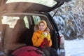 Adorable boy with hot tea or cocoa in his hands sitting in black car at winter day. Road trip at winter time