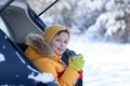 Adorable boy with hot tea or cocoa in his hands sitting in black car at winter day. Staycation travel at winter time