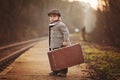 Adorable boy on a railway station, waiting for the train with suitcase and teddy bear Royalty Free Stock Photo