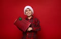 Adorable boy in Santa hat and plaid shirt holds Christmas present in glitter wrapping gift paper with green bow, smiles with Royalty Free Stock Photo