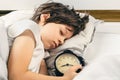 Boy sleeping peacefully and holding an alarm clock