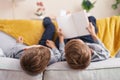Adorable boys reading book lying on sofa at home