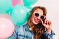 Adorable brunette young woman looking through stylish sunglasses and posing with smile next to colorful balloons. Close Royalty Free Stock Photo