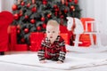 Adorable caucasian baby boy is sitting and holding gift toy Santa Claus near a Christmas tree, many festive gift boxed Royalty Free Stock Photo