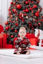 Adorable caucasian baby boy is sitting and holding gift toy Santa Claus near a Christmas tree, many festive gift boxed Royalty Free Stock Photo