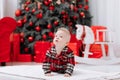Adorable caucasian baby boy is sitting and holding gift toy Santa Claus near a Christmas tree, many festive gift boxed Royalty Free Stock Photo