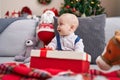 Adorable caucasian baby holding gift sitting on sofa by christmas tree at home Royalty Free Stock Photo