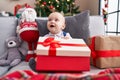 Adorable caucasian baby holding gift sitting on sofa by christmas tree at home Royalty Free Stock Photo