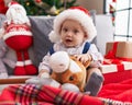 Adorable caucasian baby holding horse toy sitting on sofa by christmas tree at home Royalty Free Stock Photo