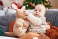 Adorable caucasian baby holding kangaroo doll sitting on sofa by christmas tree at home Royalty Free Stock Photo