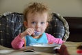 Adorable Caucasian baby sits on the table, holds a spoon and eats. Baby is very surprised. Infant`s hear is not combed. Royalty Free Stock Photo