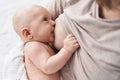 Adorable caucasian baby sitting on bed with mother sucking breast to eat at bedroom