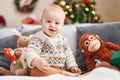 Adorable caucasian baby smiling confident sitting on sofa by christmas tree at home Royalty Free Stock Photo