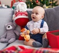 Adorable caucasian baby smiling confident sitting on sofa by christmas tree at home Royalty Free Stock Photo