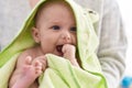 Adorable caucasian baby sucking hand wearing frog towel on mother arms at home Royalty Free Stock Photo