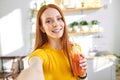 adorable caucasian female with red hair drinking juice smoothie detox and talking at smartphone camera, taking photo