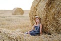 adorable caucasian girl enjoy having fun sitting near golden hay bale on wheat harvested field near farm. Royalty Free Stock Photo