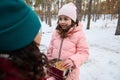 Adorable Caucasian girl in a warm pink down jacket taking a cookie out of a lunch box, enjoying a break for lunch with her loving Royalty Free Stock Photo