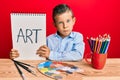 Adorable caucasian kid painter sitting at art studio holding art word depressed and worry for distress, crying angry and afraid