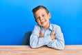 Adorable caucasian kid wearing casual clothes sitting on the table happy face smiling with crossed arms looking at the camera Royalty Free Stock Photo