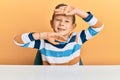 Adorable caucasian kid wearing casual clothes sitting on the table smiling cheerful playing peek a boo with hands showing face Royalty Free Stock Photo