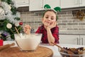 Adorable child, beautiful baby girl smiles, dreamily looking at the camera, mixing dry ingredients in a glass bowl. Cute little Royalty Free Stock Photo