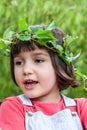 Adorable child with crown made of leaves smiling in garden