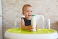 Adorable child drinking from bottle. funny baby eating healthy food on kitchen. Baby girl sitting in high chair and holding a Royalty Free Stock Photo