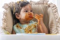 Adorable child funny girl eating spaghetti with spoon while sitting in high-powered chair at home. Toddler child with Royalty Free Stock Photo