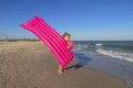 Adorable child girl with pink inflatable air mattress on wild empty sea beach