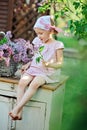 Adorable child girl in pink plaid dress sit on vintage bureau with lilacs in basket Royalty Free Stock Photo