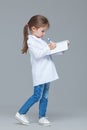 Adorable child girl uniformed as doctor is writing medical record isolated on grey background