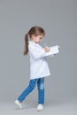 Adorable child girl uniformed as doctor is writing medical record on grey background