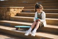 Adorable child girl using mobile phone, browses internet, plays online video games, watches cartoons, sitting on steps