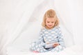 Adorable child in pajamas sitting on bed with crossed legs and writing