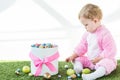 Child in pink fluffy costume sitting on green grass near box with colorful Easter eggs isolated on white Royalty Free Stock Photo