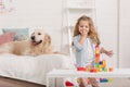 adorable child playing with educational cubes, golden retriever lying on bed