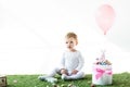 Child sitting on green grass near box with colorful quail eggs, decorative rabbit and air balloon isolated on white Royalty Free Stock Photo